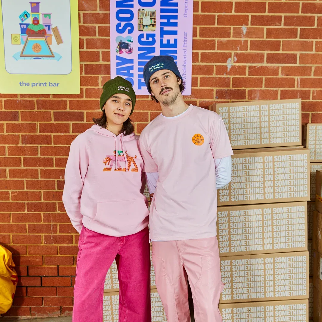 Two people in pink hoodies and sweatshirts stand near boxes at The Print Bar's Melbourne location