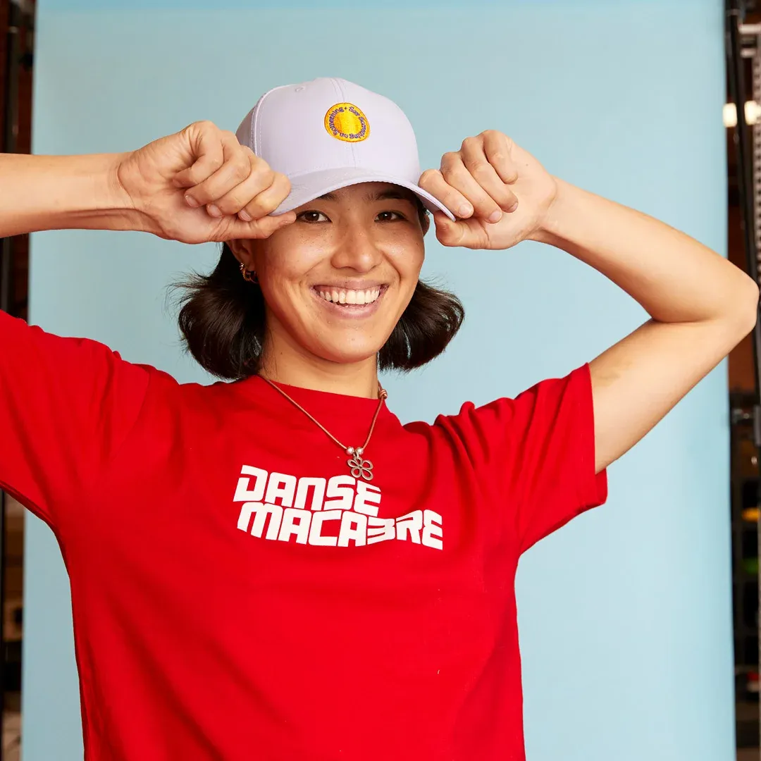 A person is smiling wearing a personalised screen printed t-shirt and a pink embroidered cap with a logo