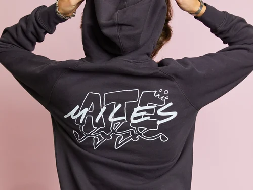 A person seen from behind, wearing a black hoodie with the phrase "ATE MILES" in white, stands in front of a pink background