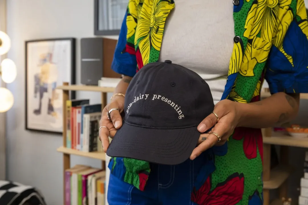 A person in their apartment is holding a cap embroidered with a custom logo