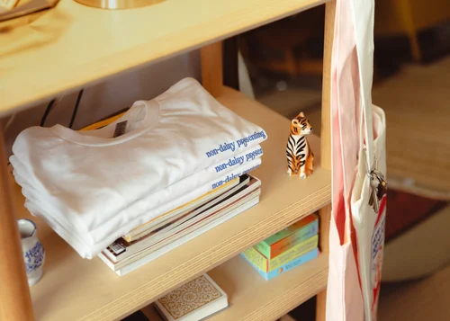A stack of white screen printed t-shirts sits neatly stacked on a shelf.