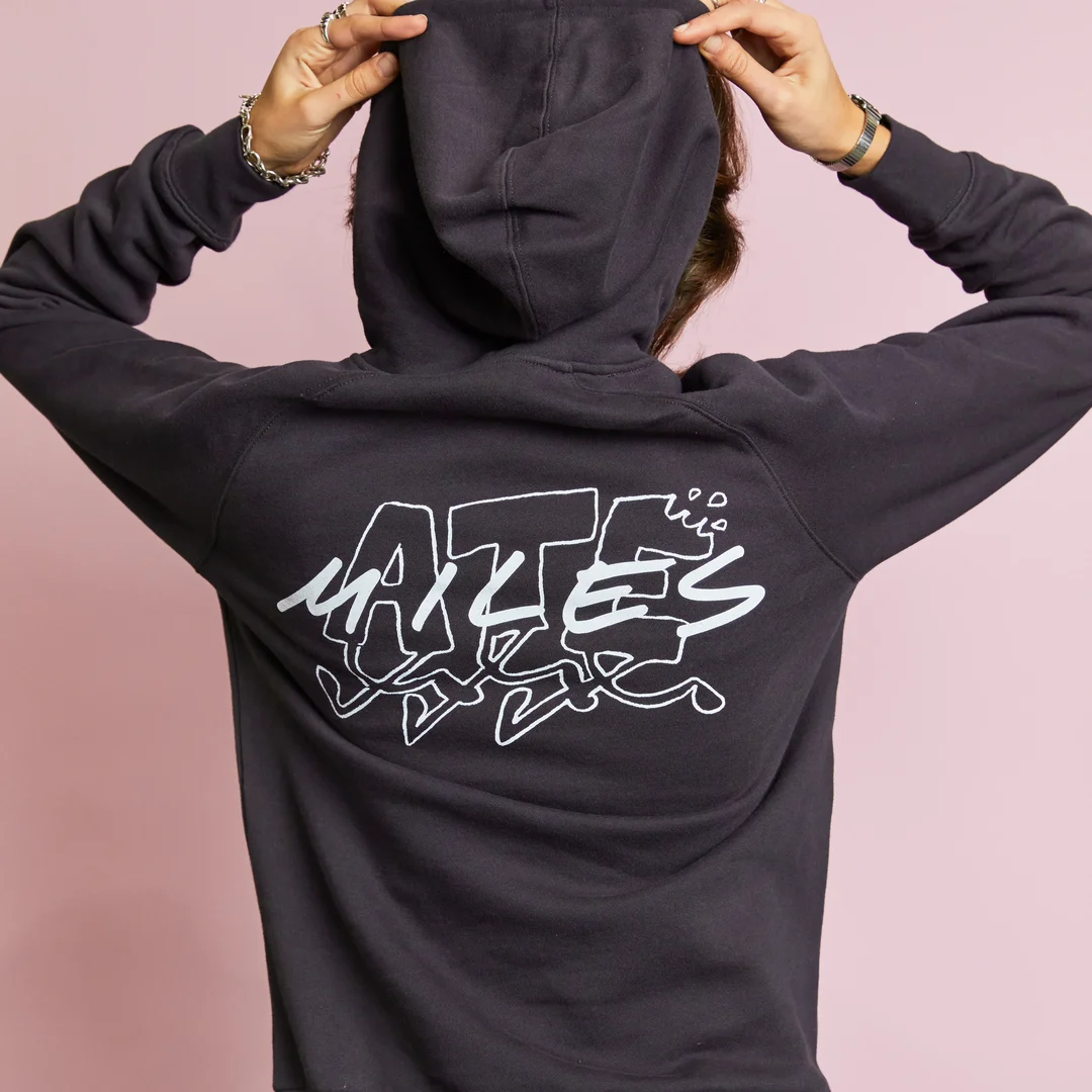 A person seen from behind, wearing a black hoodie with the phrase "ATE MILES" in white, stands in front of a pink background