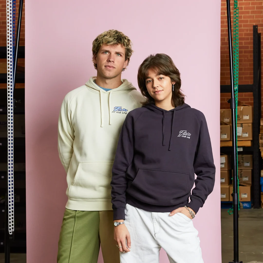 Two people stand infront of a colour roll. They are both wearing custom digitally printed hoodies