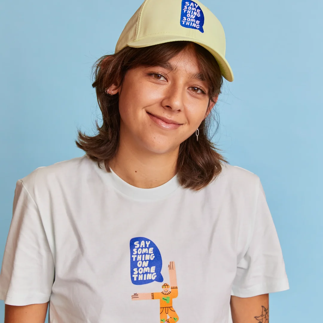 A person is smiling wearing a personalised digital printed white t-shirt with a logo and an embroidered cap with a design