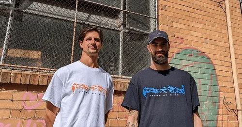 Two men stand in front of a building wearing 'Frame of Mind' T-shirts