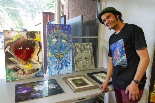 A person stands in front of a row of artworks smiling