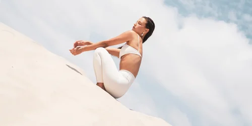 Woman wearing white activewear posing on a sandy slope under a bright sky